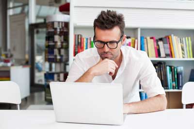 Man with glasses reading from laptop computer screen