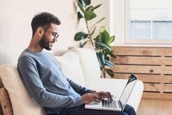 man with glasses sitting on couch with laptop computer