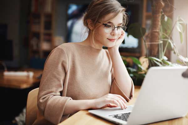 woman with glasses scrolls through document on laptop computer